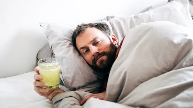 Man holding a drink while lying in bed at home