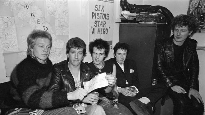 Sex Pistols brandish their £25,000 pay off cheque from A&M Records, while manager Malcolm McLaren looks on. March 1977