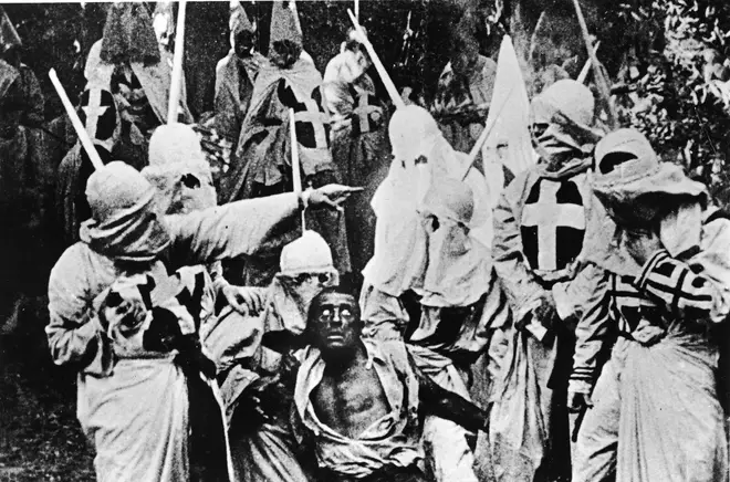 Actors costumed in the full regalia of The Ku Klux Klan surround a white actor in blackface in The Birth Of A Nation