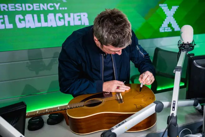 Noel signs the guitar in the Radio X studio