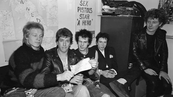 Sex Pistols brandish their £25,000 pay off cheque from A&M Records, while manager Malcolm McLaren looks on. March 1977