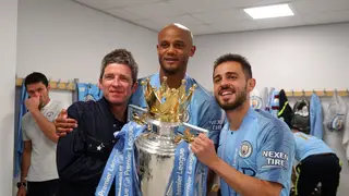 Noel Gallagher, Vincent Kompany and Bernardo Silva of Manchester City celebrate with trophy in the Manchester City dressing room after winning the Premier League title